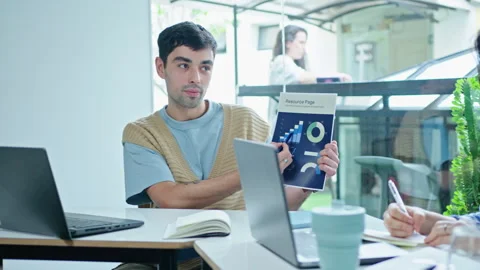 Gen Z Man Explaining Business Graphs on Paper to Colleagues on Meeting Stock-Footage 243945296