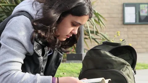 Gender neutral kid reading book outside school Stock Footage 155387519
