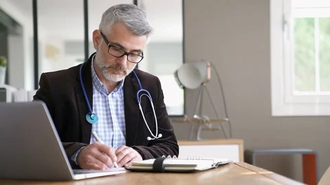 General practitioner sitting at his desk in medical office Stock Footage 103287270