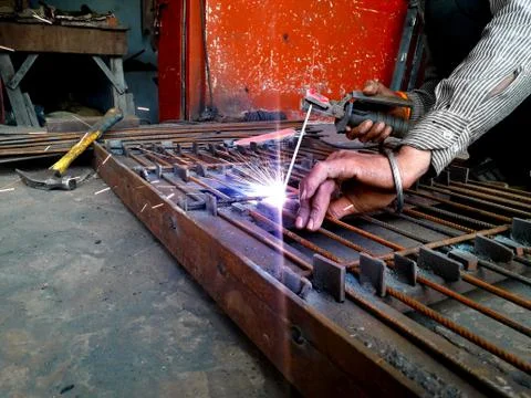 Generating blue sparks while worker welding on iron in industrial workshop Stock Photos