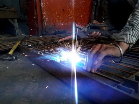 Generating blue sparks while worker welding on iron in industrial workshop Stock Photos