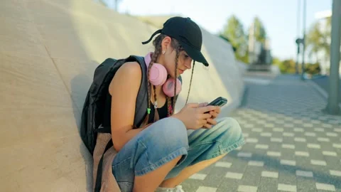 Generation Alpha, Adolescent sitting outdoors using mobile phone near street Stock Footage 340479386