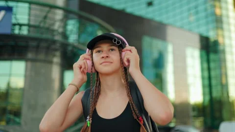 Generation Alpha, Adolescent standing outdoors putting pink wireless headphones Stock Footage 340479122