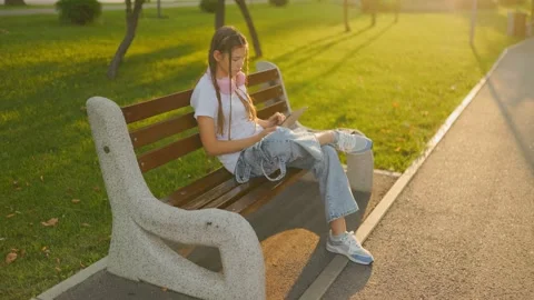 Generation Z teen using mobile tablet on park bench during sunset. Stock Footage 340924788