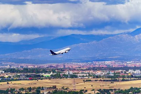 Generic Avio taking off and taking height next to a city and large mountains in Stock Photos