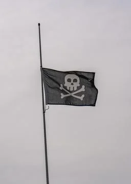 A generic pirate flag flutters in the wind against the sky.Skull and bones Stock Photos