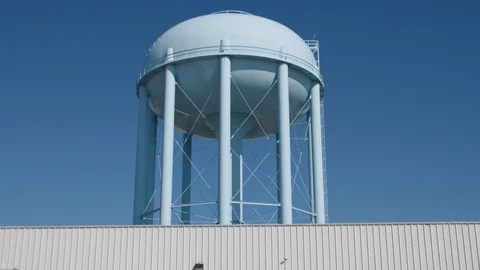 Generic Water Tower with No Logos Over Large Factory, tilt up shot on sunny day Stock Footage 125913829