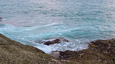 Gentle blue waves flowing through rocky shoreline formations. Video stock 333874580