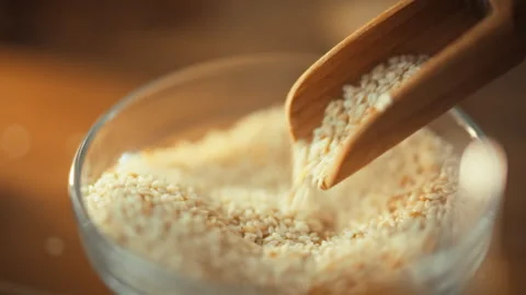 With gentle hand gesture man pours sesame seeds from special spoon into glas Stock Footage 331365568