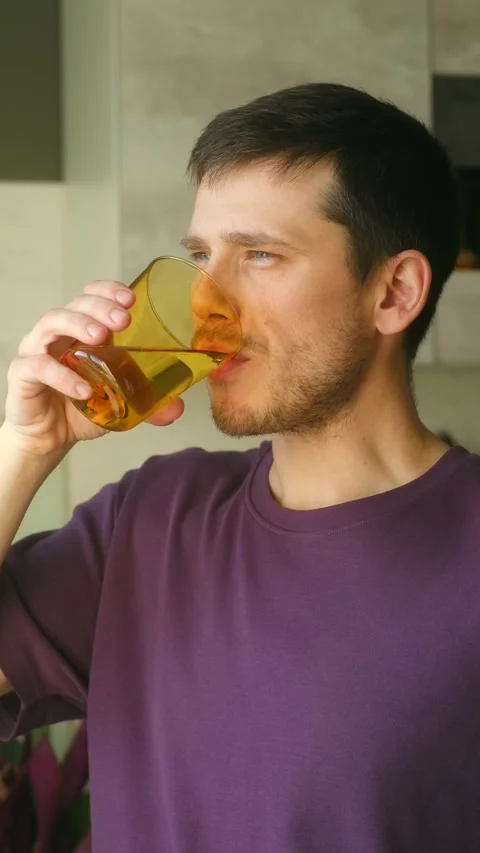Gentle morning hydration routine, Man enjoys slow sip of water in kitchen light Stock Footage 337547607
