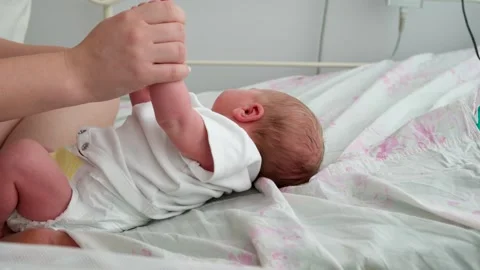 Gentle mother's hands hold the tiny hands of her crying newborn baby, providing Stock Footage 344772006