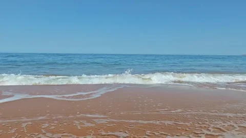A gentle ocean wave rolling onto a sandy beach under a clear blue sky Stockbeeldmateriaal 334084904