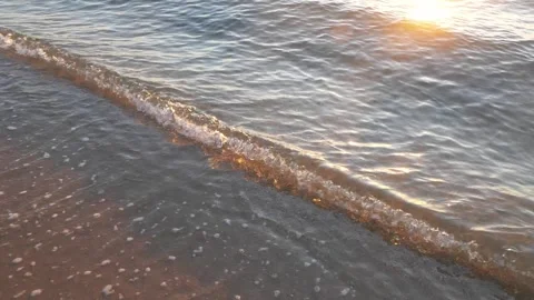Gentle ocean wave rolling onto sandy shoreline during warm sunset Stock Footage 337409335