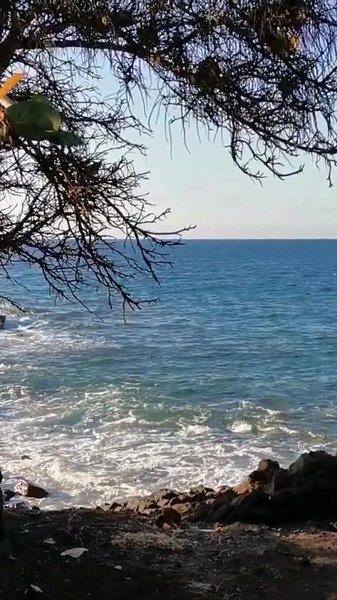 Gentle ocean waves breaking on a rocky shoreline viewed through the silhouette Stock Footage 344786103