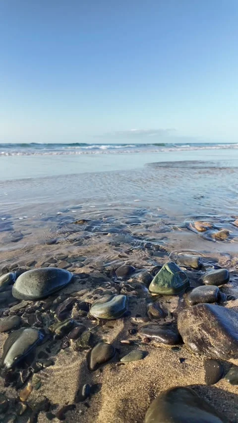 Gentle ocean waves caressing a sandy and pebbled shore Stock Footage 345839147