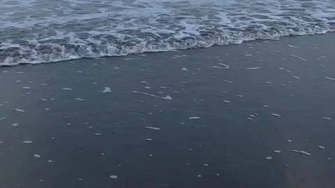 Gentle ocean waves lap onto dark wet sand with foam trails. Stock Footage 344243895