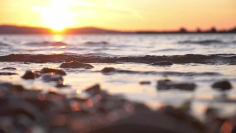 Gentle ocean waves lap rocky shore under glowing golden sunset Stock Footage 343234858