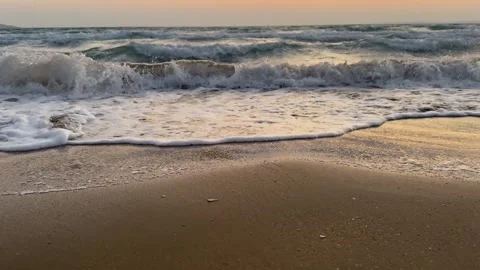 Gentle ocean waves lap sandy beach at sunset, wide shot Stock Footage 345166730