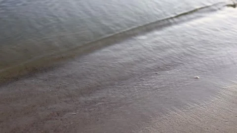 Gentle ocean waves lap onto a sandy beach in soft natural light Stock Footage 345364957