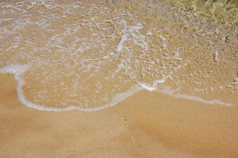 Gentle ocean waves lapping against sandy beach shoreline under sunlight Stock Photos