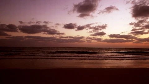 Gentle ocean waves roll onto a quiet sandy beach during a stunning sunset. 库存影片 341468617