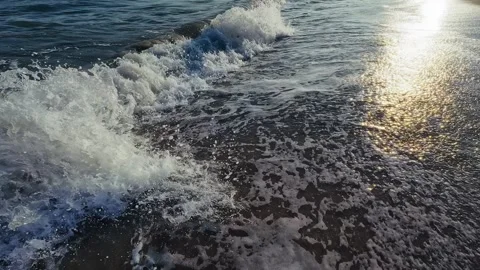 Gentle ocean waves roll onto sandy shore with shimmering sunlight reflections Stock Footage 326243482
