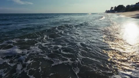 Gentle ocean waves roll onto sandy shore with shimmering sunlight reflections Stock Footage 326243536
