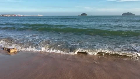 Gentle ocean waves roll onto sandy shore with distant islands lighthouse and Stock Footage 326716407