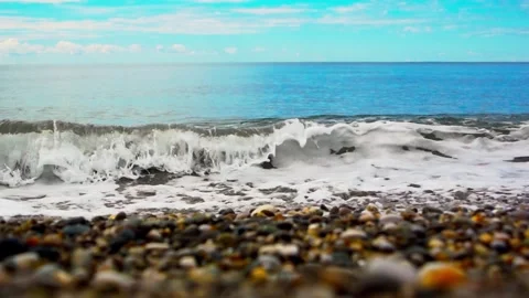 Gentle ocean waves rolling onto pebble beach under bright blue sky with sca.. Stock-Footage 347884741