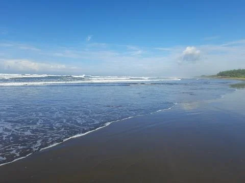 Gentle ocean waves rolling onto a sandy beach shore Stock Photos