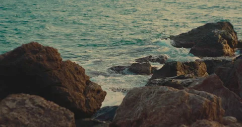 Gentle ocean waves washing around dark rugged rocks at the shore. Stock Footage 342469742