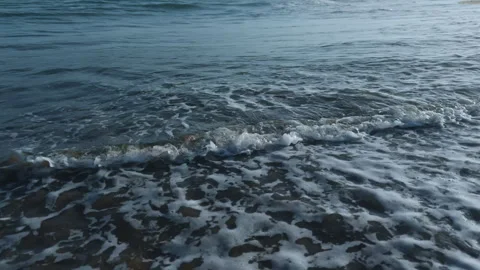 Gentle ocean waves washing over sandy beach with a trail of human footprints Stock Footage 337418937