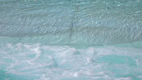 Gentle ocean waves washing up on a sandy beach with clear water in 4K Stock Footage 283459934