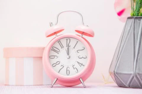Gentle pink alarm clock next to a vase of flowers and a decorative gift box Stock Photos
