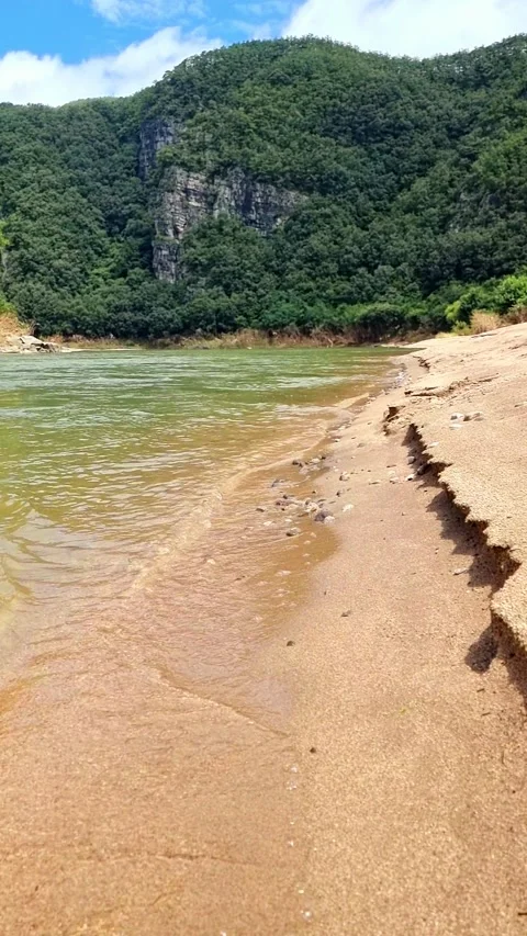 Gentle River Waves Shaping Sloped Sand Beneath a Blue Mountain Stock Footage 328299064