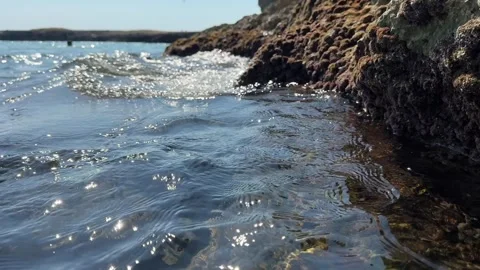 Gentle sea waves flow along a rugged rocky coastline with textured cliffs and cl Stock Footage 340330331