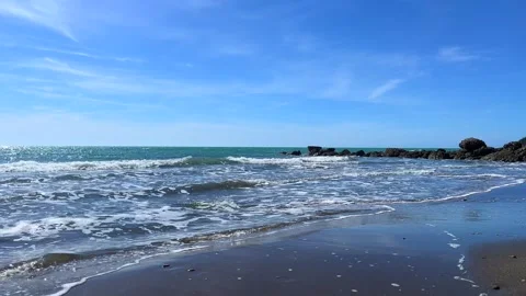 Gentle sea waves rolling onto sandy shore under blue sky Stock Footage 310242744