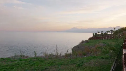 Gentle sunset over tranquil waters with lush palms and distant mountains in view Vídeo Stock 331531383