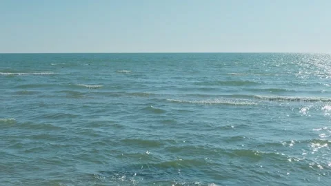 Gentle turquoise waves of the sea, glared by the sun against a blue sky. Ge.. Video stock 330014319