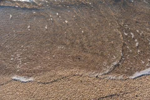 A gentle wave washes over fine sand, creating delicate patterns in the sunl.. Stock Photos