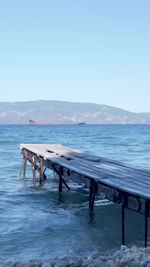 Gentle waves are hitting an old wooden pier, while a cargo ship is sailing in Stock-Footage 294963992