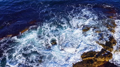 Gentle waves caressing rugged rocks along a serene coastline at sunset, captured Stock Footage 332065544
