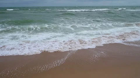 Gentle waves lapping against the sandy shore during an overcast day at the beach Stock Footage 285187116