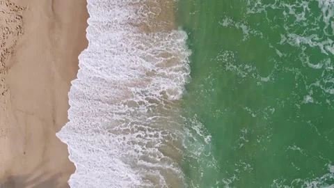 Gentle waves lapping against a sandy beach under bright sunlight in a coastal Stock Footage 285645596
