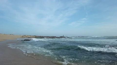 Gentle waves lapping on sandy beach, man fishing in distance Video stock 194201255