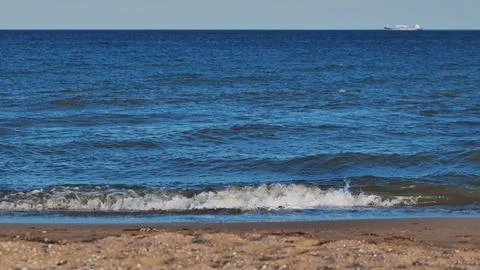Gentle waves lapping on sandy beach with cargo ship sailing on horizon of black Stock Photos