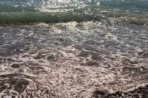 Gentle waves lapping the shore create a serene scene at the beach. Sunlight s Stock Photos