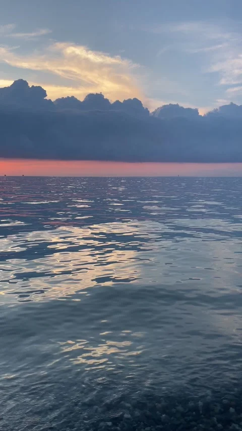 Gentle waves ripple across the open sea beneath dramatic blue storm clouds .. Stock Footage 338237083