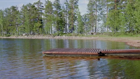 Gentle waves ripple around a rustic wooden dock along a peaceful lake shoreline. Stock Footage 344903174
