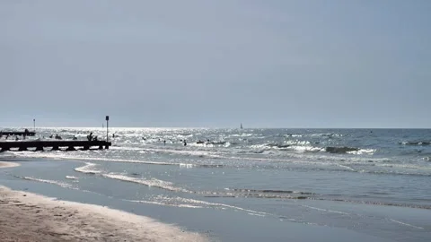 Gentle waves roll onto a quiet beach under a hazy sky Stock Footage 313844948